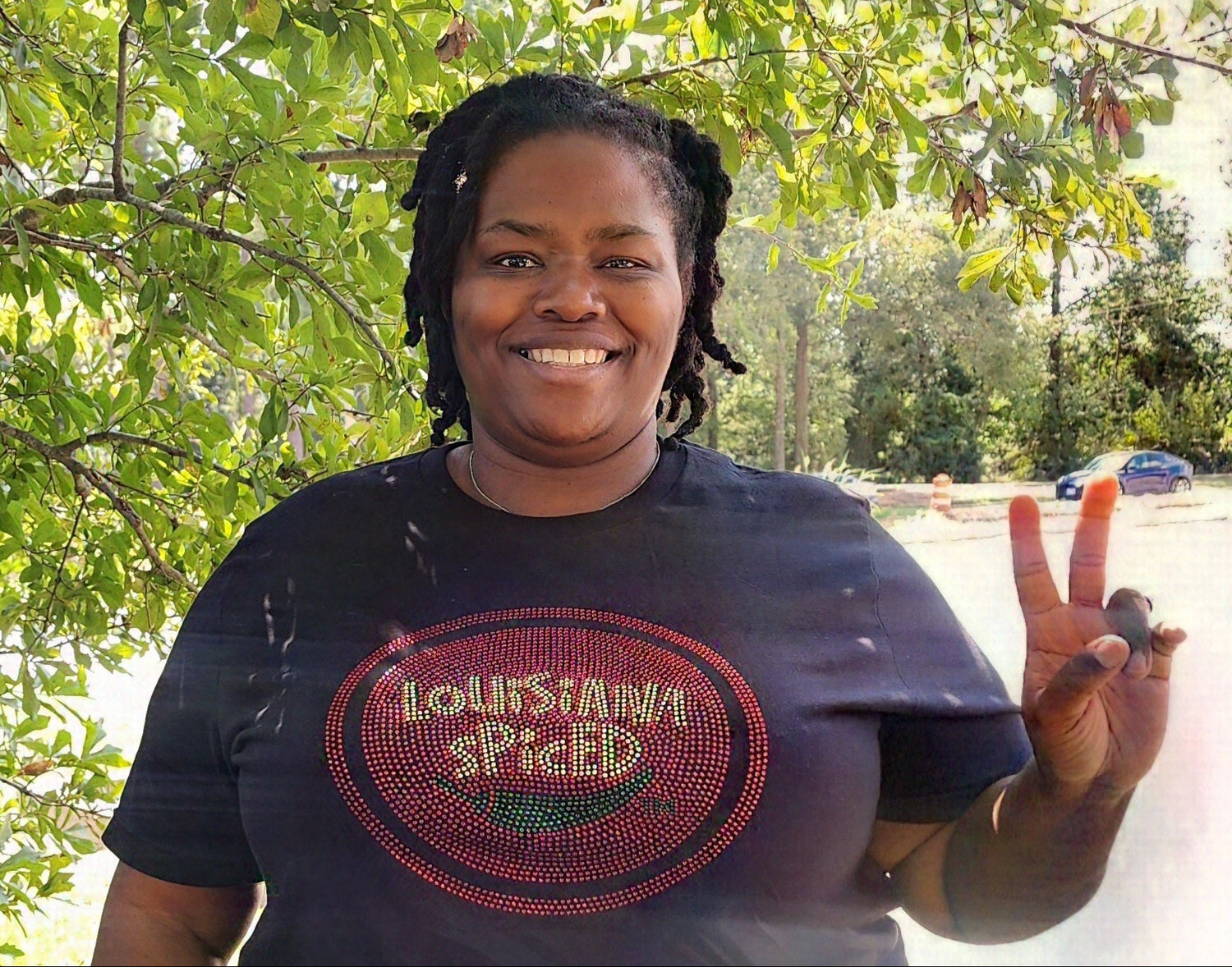 Person wearing a 'Louisiana Spiced' t-shirt outdoors with trees in the background
